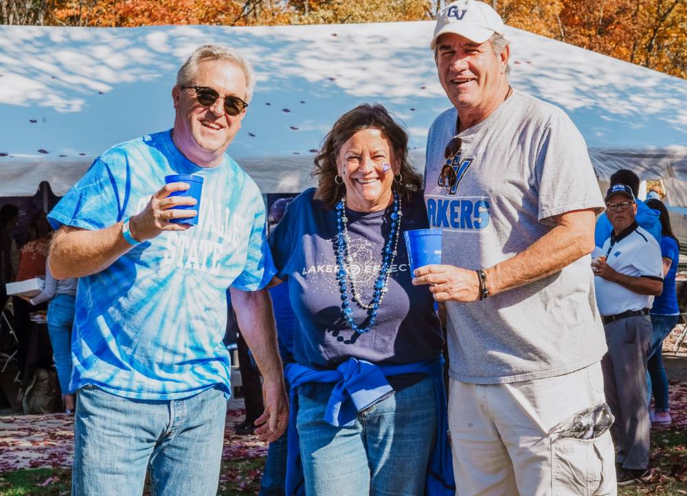 Three alumni standing together at the tailgate.